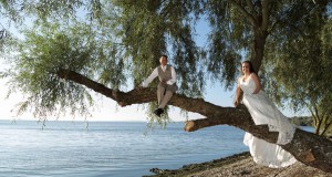 Brautpaar sitzt auf Baum vor Seepanorama